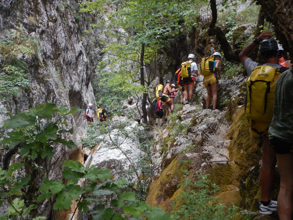 Ομάδα με κράνη και σακίδια κινείται σε βραχώδες πέρασμα με μεταλλικά πατήματα και συρματόσχοινο