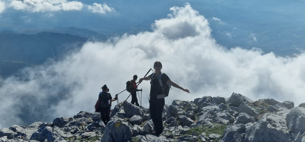Τρεις πεζοπόροι σε βραχώδη ορεινή κορυφή με σύννεφα πάνω από τις γύρω πλαγιές
